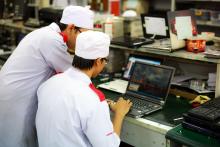 Two technicians in uniforms working on laptops in a laboratory setting